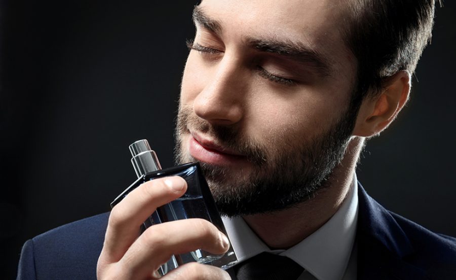 Handsome man in formal suit and with bottle of perfume on dark b