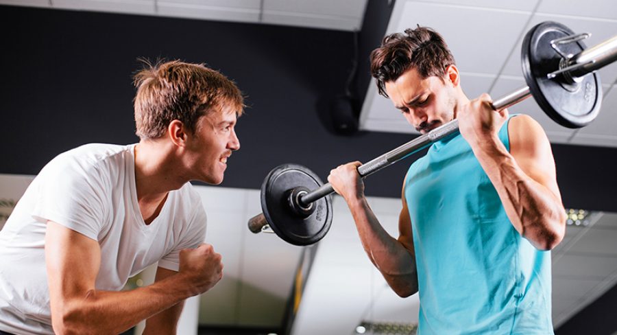 Young man motivating gym buddy during bicep exercise