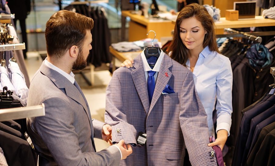 Confident handsome man with beard choosing a jacket in a suit sh
